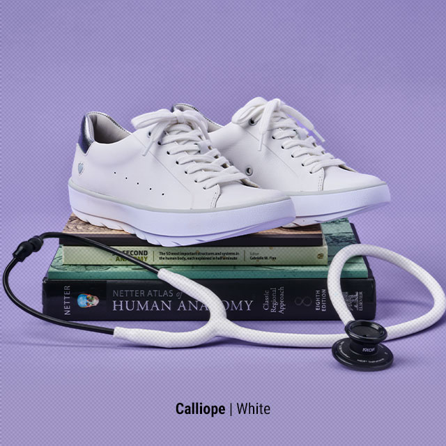 Calliope | White. Calliope sneakers sitting on top of medical books.